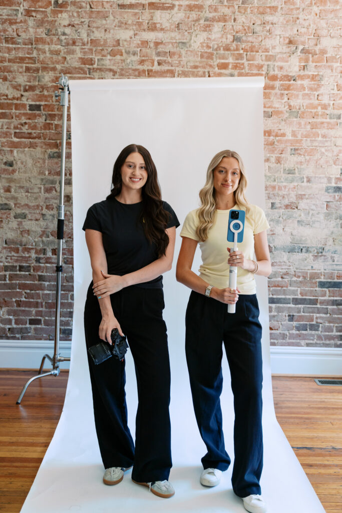 Two content creators holding a camera and phone gimbal on a white studio backdrop