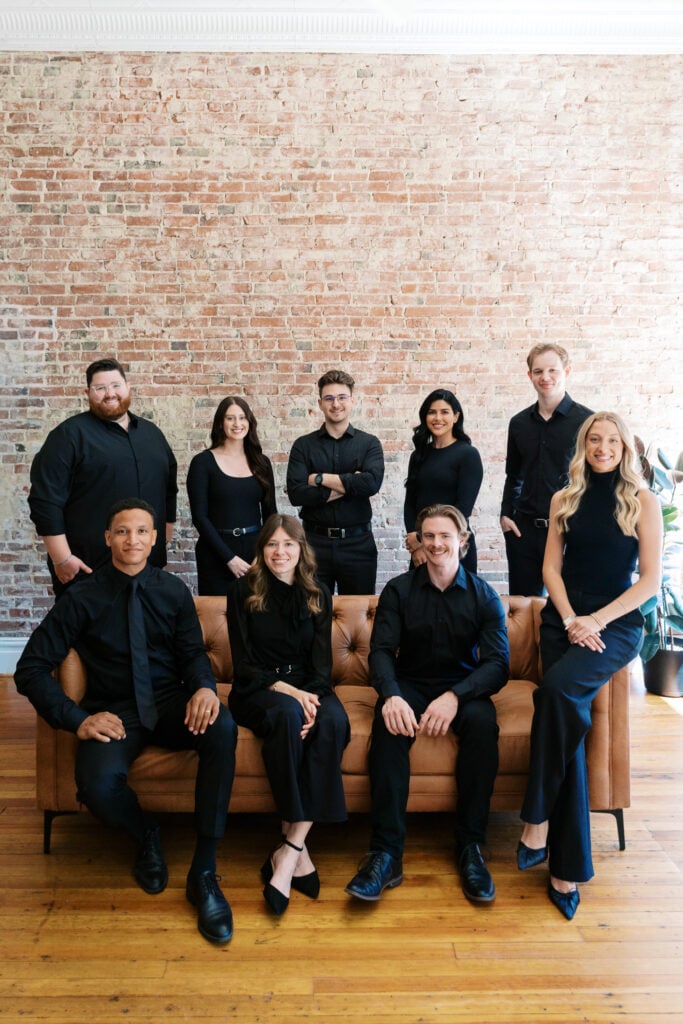 Full Posted Social team in black gathered around a leather sofa against an exposed brick wall