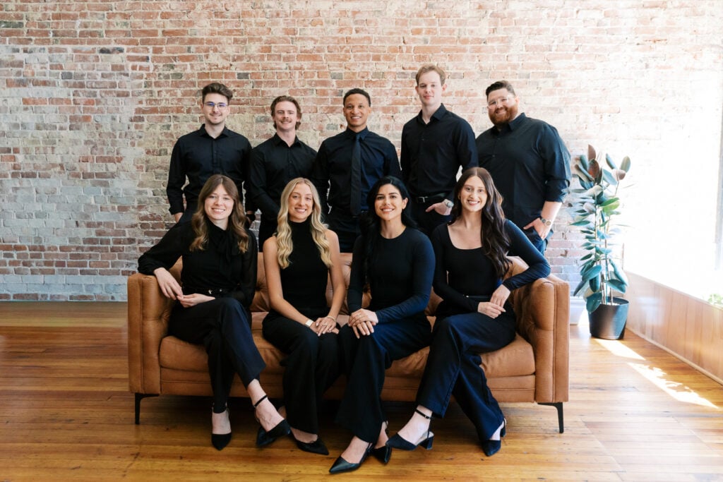 Wide shot of the full Posted Social team around a leather sofa in the brick-walled studio