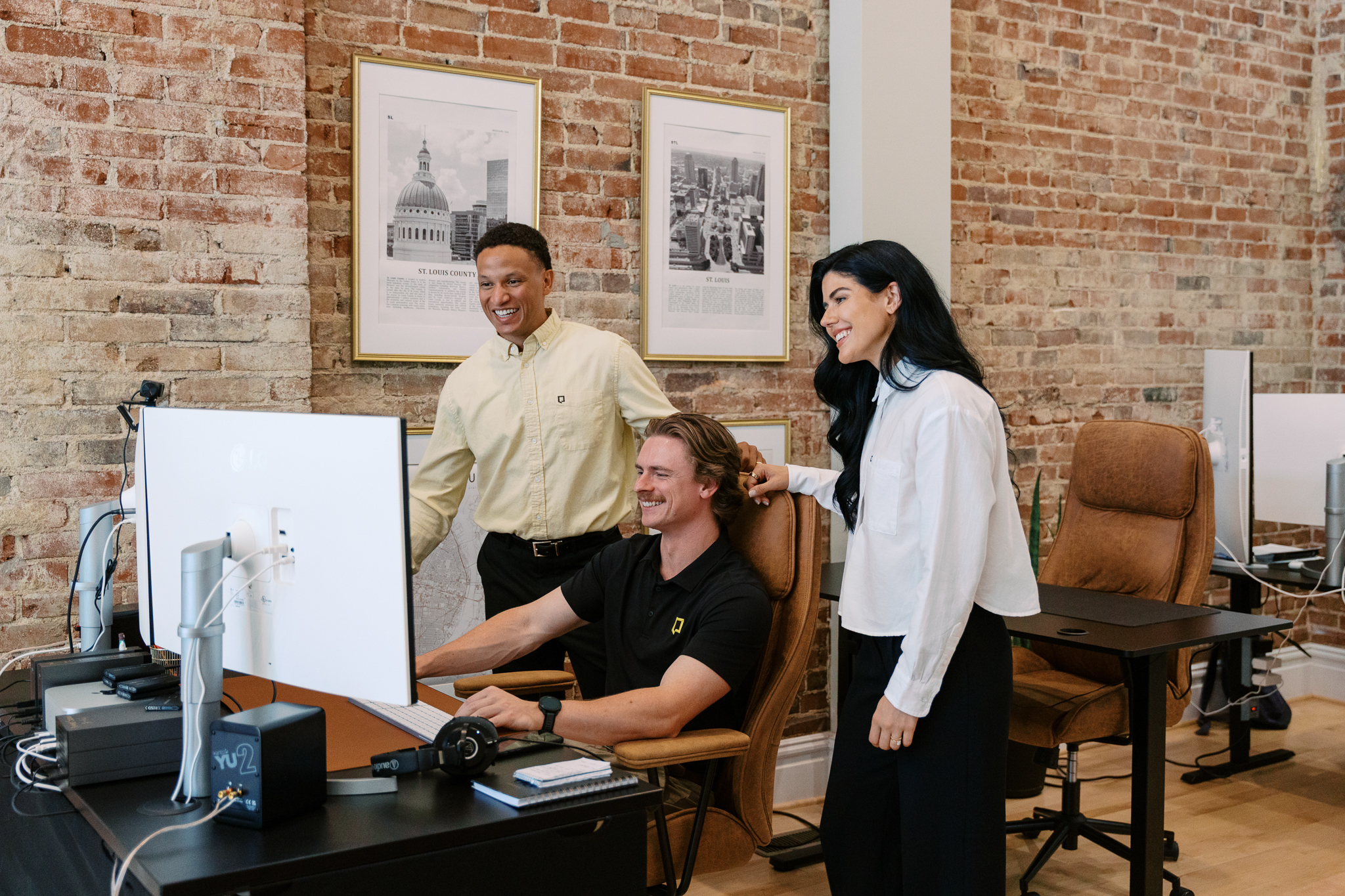 Three team members collaborating at a desk beneath framed vintage St. Louis prints