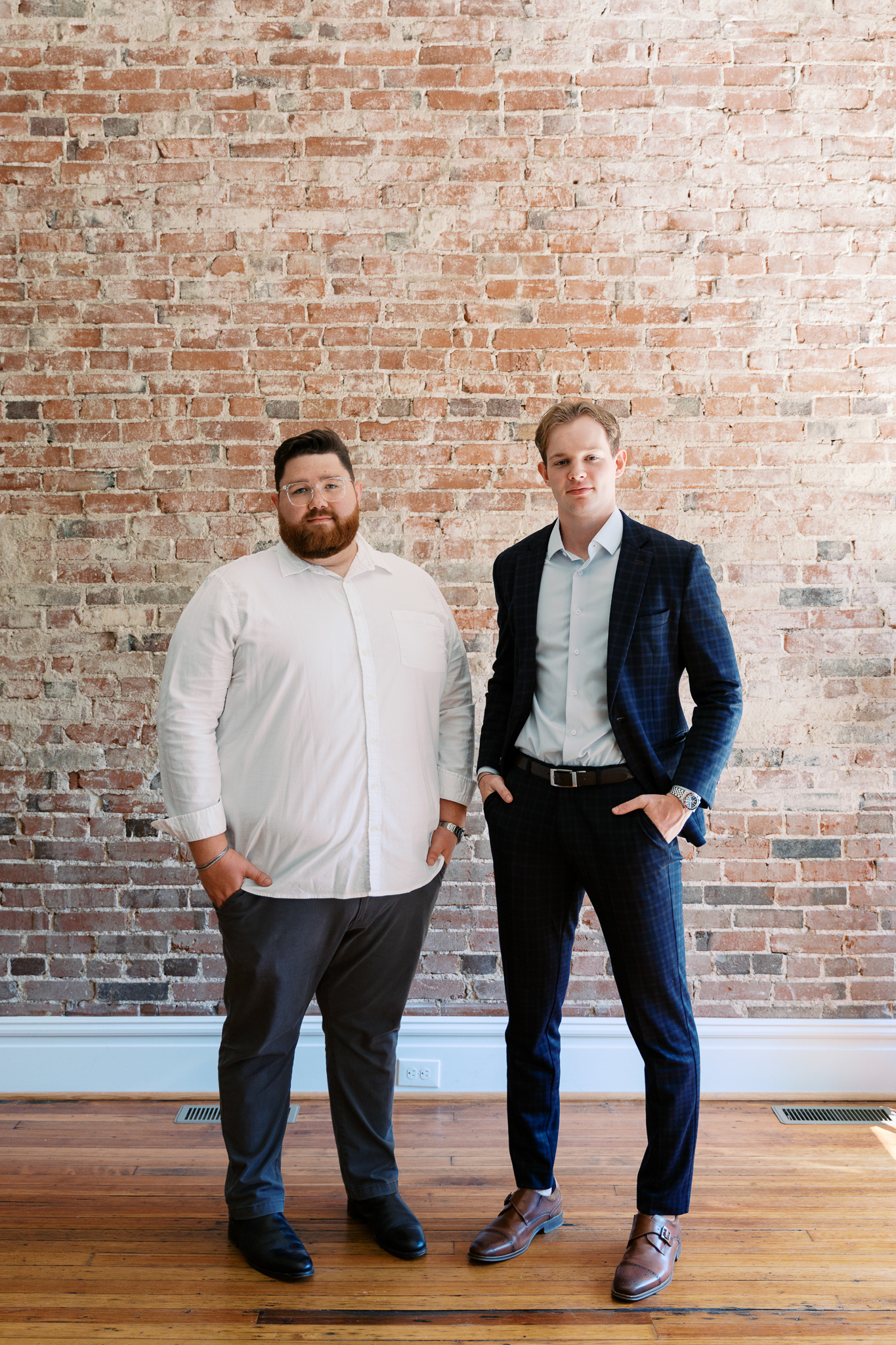 Two team members in business attire standing against an exposed brick wall
